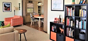 Een woonkamer met een bank, een salontafel, een boekenkast en een eethoek met een tafel en stoelen.