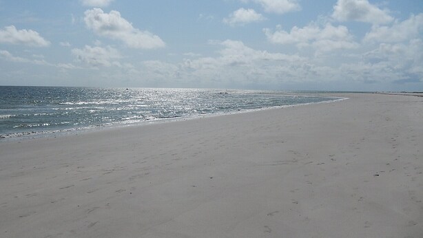 Una playa extensa de arena clara, con olas suaves y cielo despejado.