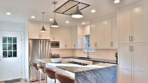 Una cucina moderna con mobili bianchi, elettrodomestici in acciaio inossidabile, un'isola in marmo e luci a sospensione.