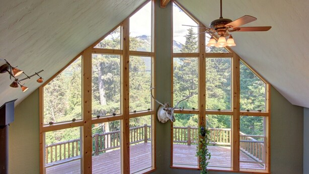 Ein Zimmer mit großen Fenstern, einem Deckenventilator und einer Holzterrasse draußen.