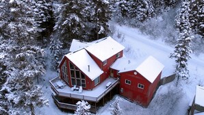 Eine rote Holzhütte mit einer Terrasse, umgeben von schneebedeckten Bäumen.