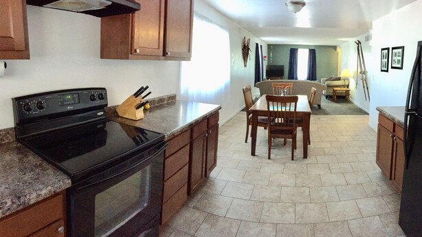 A kitchen with granite countertops, wooden cabinets, a black stove, and a dining area with a table and chairs.