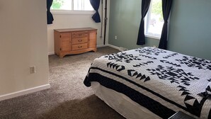 A bedroom with a bed, a dresser, and two windows with curtains.