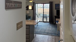 Een moderne hotelkamer met een welkomstbord, een plafondventilator, een groot raam, een eethoek en uitzicht op de oceaan.