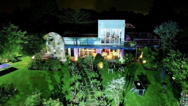 A modern house with a glass facade, surrounded by a well-maintained garden and a swimming pool.
