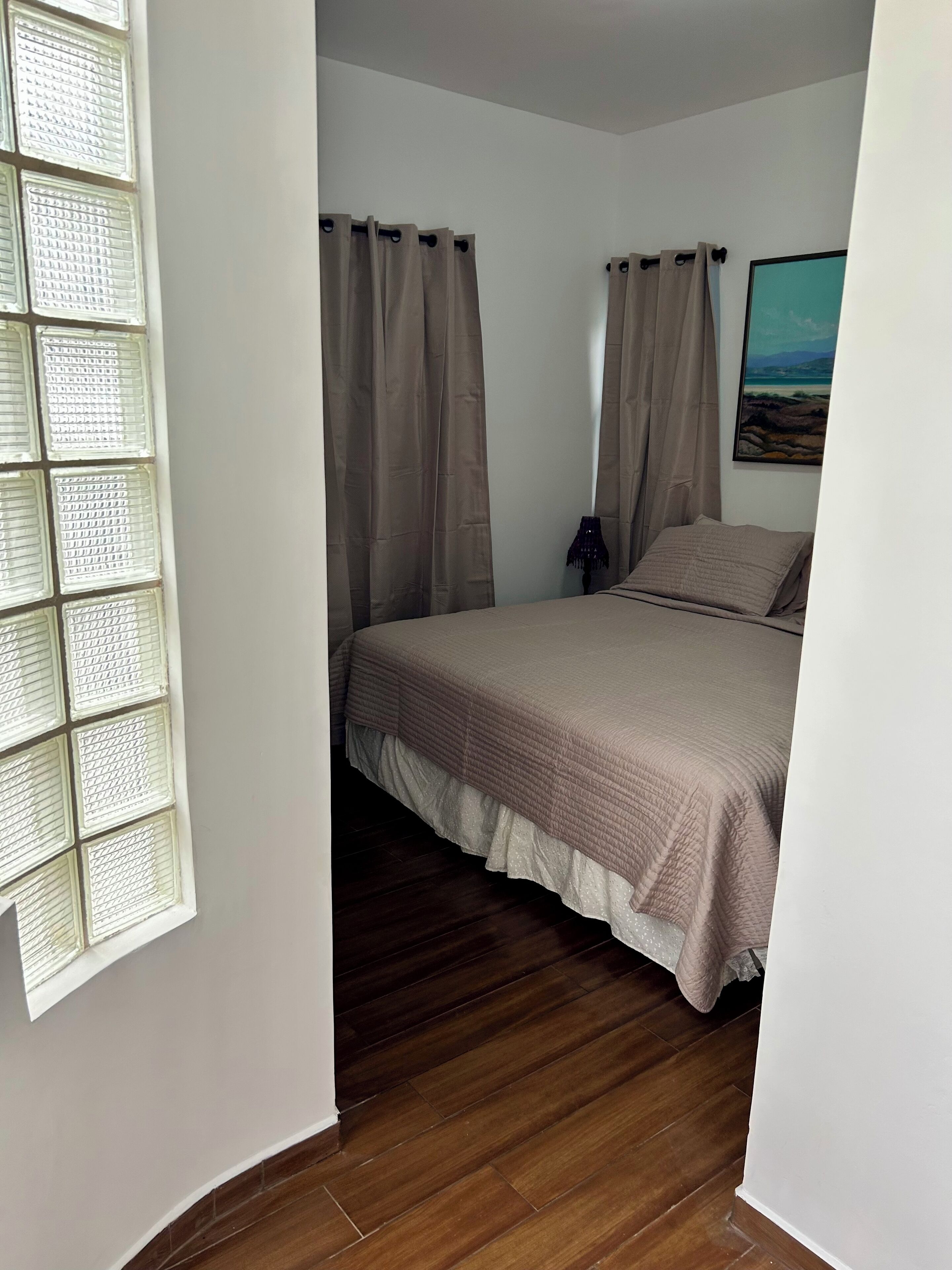 A bedroom with a bed, curtains, a nightstand, and a painting on the wall.