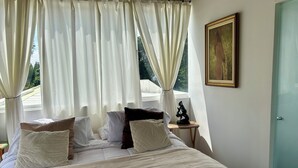 A neatly made bed with white bedding and multiple pillows, a small bedside table with a sculpture, and a painting on the wall.