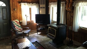 Un intérieur de chalet chaleureux, avec un revêtement mural en bois, une cheminée, un téléviseur et un coin salon confortable.