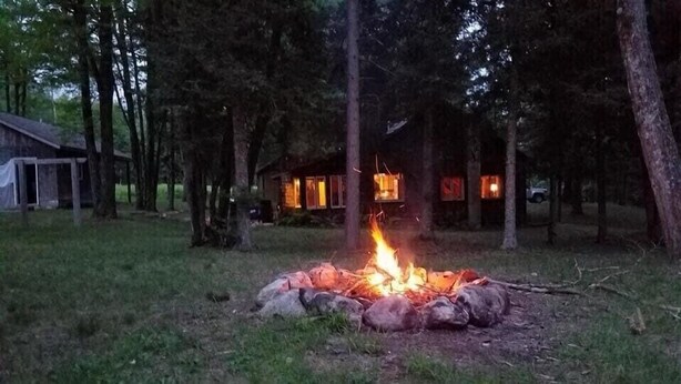 Un feu de camp dans une zone boisée, avec un chalet en arrière-plan.