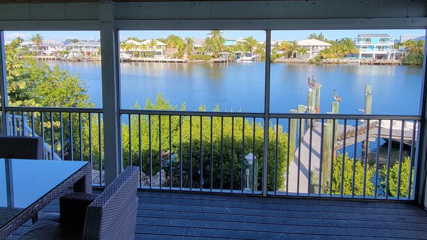 A covered outdoor area with a view of a lake, wooden deck, and a railing. - Manatee Bay , Pool table, Pool, Kayaks, Jacuzzi not working.  (Marathon)