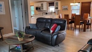 A spacious living room with a black leather sofa, a wooden coffee table, and a dining area with wooden chairs and a table. - Manatee Bay , Pool table, Pool, Kayaks, Jacuzzi not working.  (Marathon)