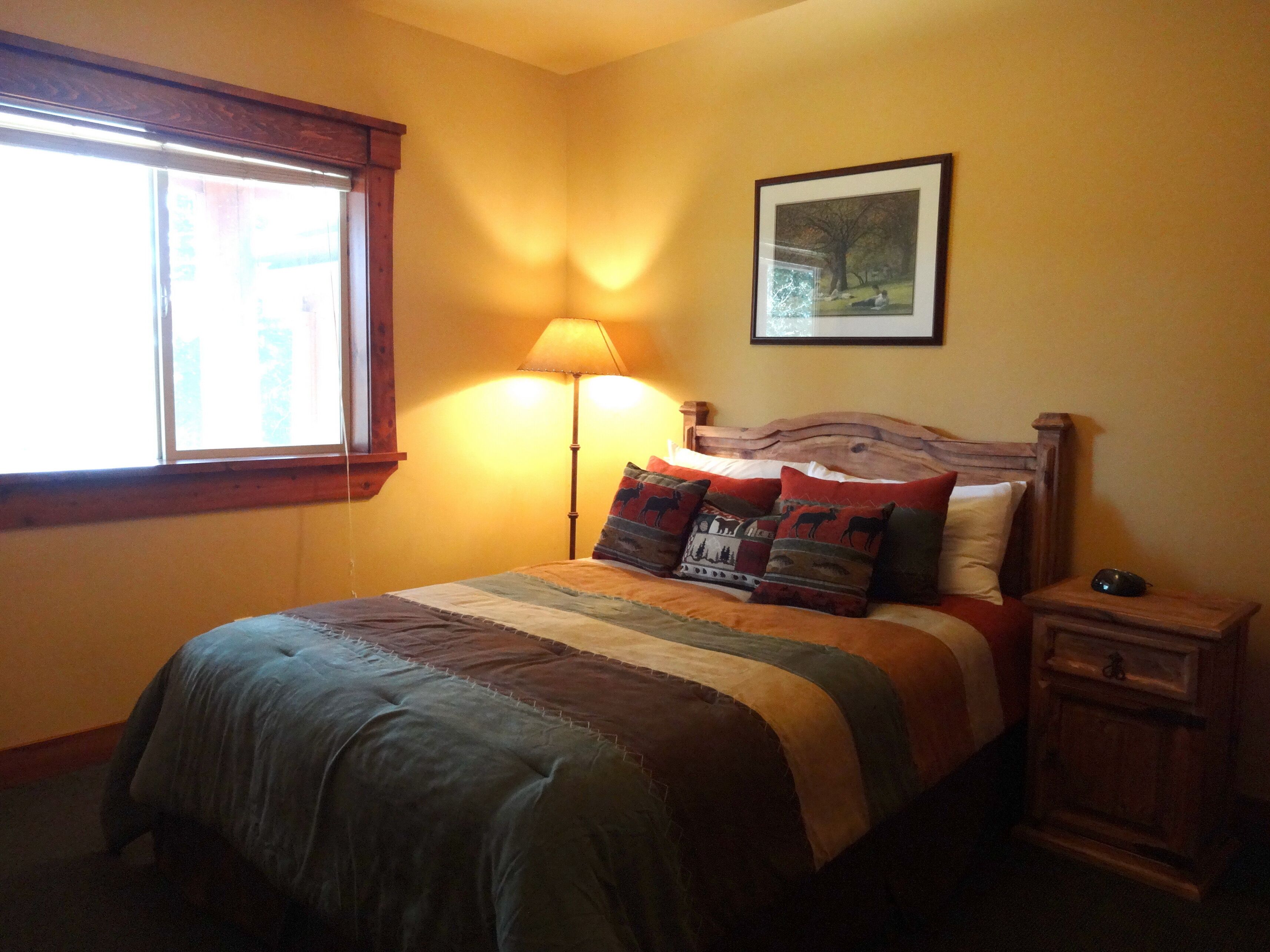 A bedroom with a bed, a nightstand, a lamp, and a window.