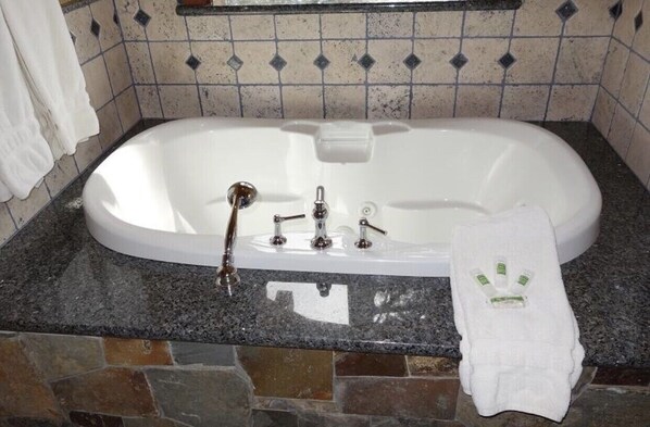 A bathroom with a white bathtub, a granite countertop, and a tiled wall with a diamond pattern.