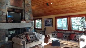 A cozy living room with a stone fireplace, wooden ceiling, and a large window. - Tahoe Ski Lodge  WiFi, hot-tub sleeps 12 (Truckee)