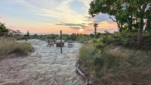 A beach setting with a wooden bench and a table, surrounded by sand and vegetation. - On Beach, Sunsets, Bikes+Kayaks, Pet Friendly, Firepit, Serenity.  (Villas)