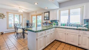 A kitchen with white cabinets, a green and white tiled countertop, a dining table with chairs, and a ceiling fan. - On Beach, Sunsets, Bikes+Kayaks, Pet Friendly, Firepit, Serenity.  (Villas)