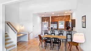A modern kitchen with a brick accent wall, a dining area with a wooden table and chairs, and a staircase leading to another level. - Brewers Perch Vacation Rental - Walking To Watkins Glen Attractions (Watkins Glen)