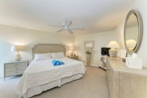 A hotel room with a bed, a nightstand, a dresser, a mirror, a ceiling fan, and a vase with flowers. - Sea Grape Inn #5- Beachfront Property (Longboat Key)