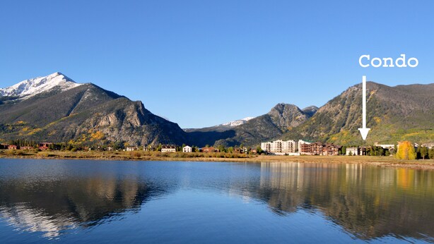 Un lac paisible, avec des montagnes en arrière-plan et un immeuble d’appartements indiqué par une flèche.