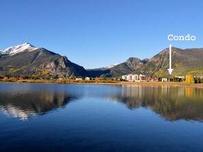 Ein ruhiger See mit Bergen im Hintergrund und einer mit einem Pfeil markierten Eigentumswohnung.