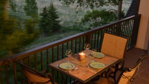 Un balcon avec une table dressée pour deux personnes, offrant une vue panoramique sur un paysage magnifique, avec des montagnes et un lac.
