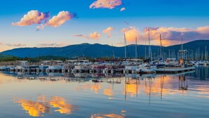 Un port de plaisance avec des bateaux amarrés, une eau calme et des montagnes en arrière-plan.