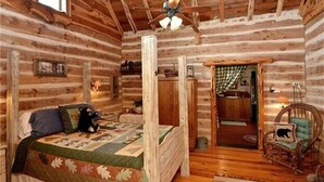 A log cabin bedroom with a bed, a chair, a ceiling fan, and a door leading to another room. - 16-Acre Resort Ranch with 4 Homes Included, Pool, Spa, Firepit &Gathering Spaces (Kyle)