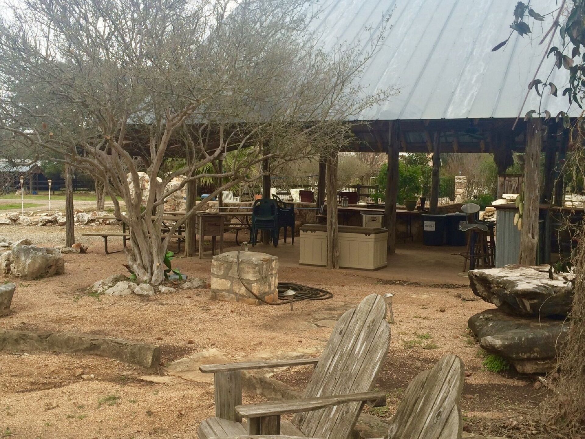 Un espace extérieur aménagé avec des tables et des chaises en bois, des jardinières en pierre et un espace abrité doté de tabourets de bar.