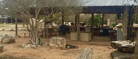 Un espace extérieur aménagé avec des tables et des chaises en bois, des jardinières en pierre et un espace abrité doté de tabourets de bar.