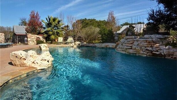 A clear blue pool surrounded by stone walls and a few trees. - 16-Acre Resort Ranch with 4 Homes Included, Pool, Spa, Firepit &Gathering Spaces (Kyle)