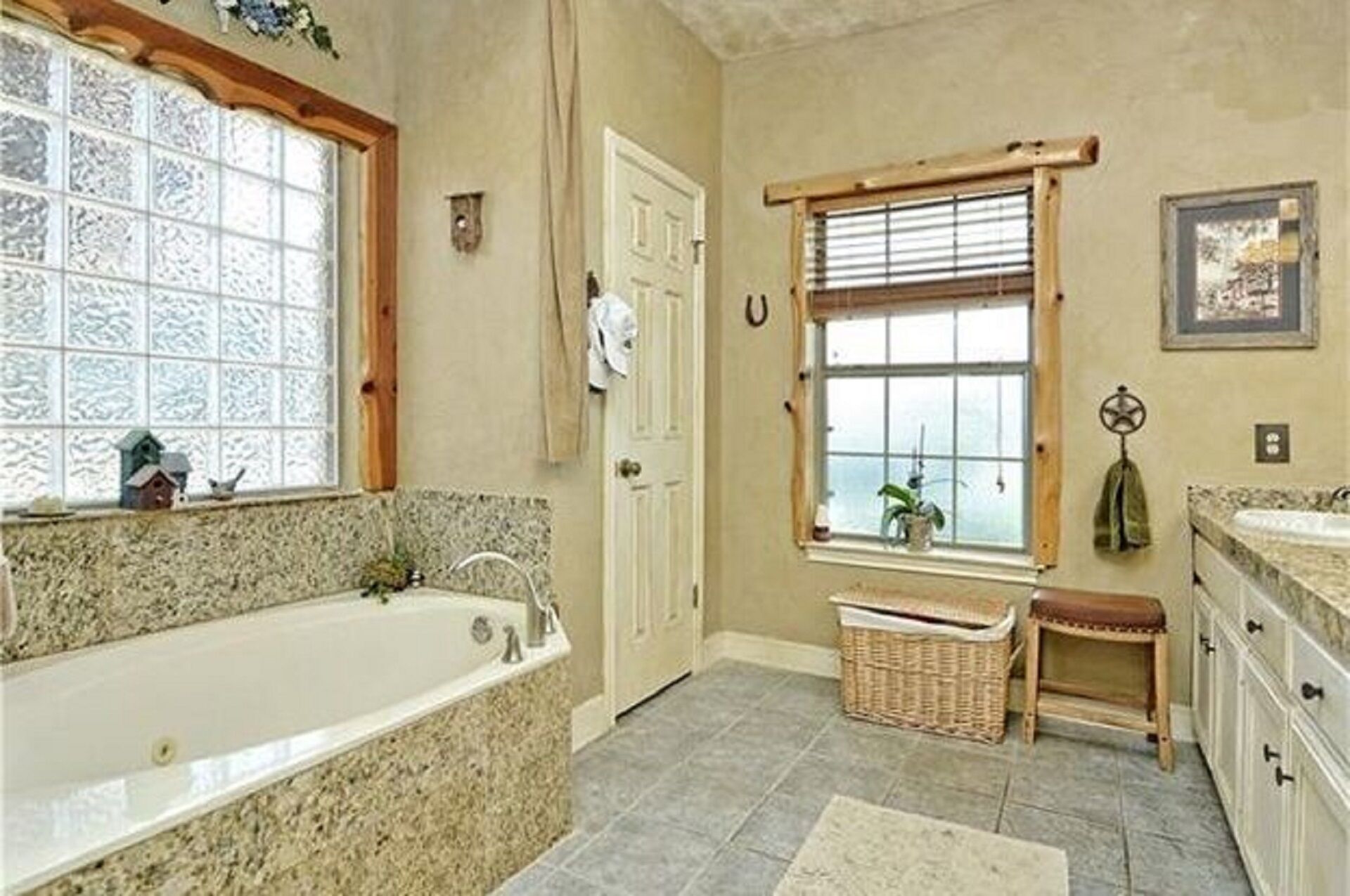 A bathroom with a large bathtub, a window with blinds, a wicker basket, and a small stool.