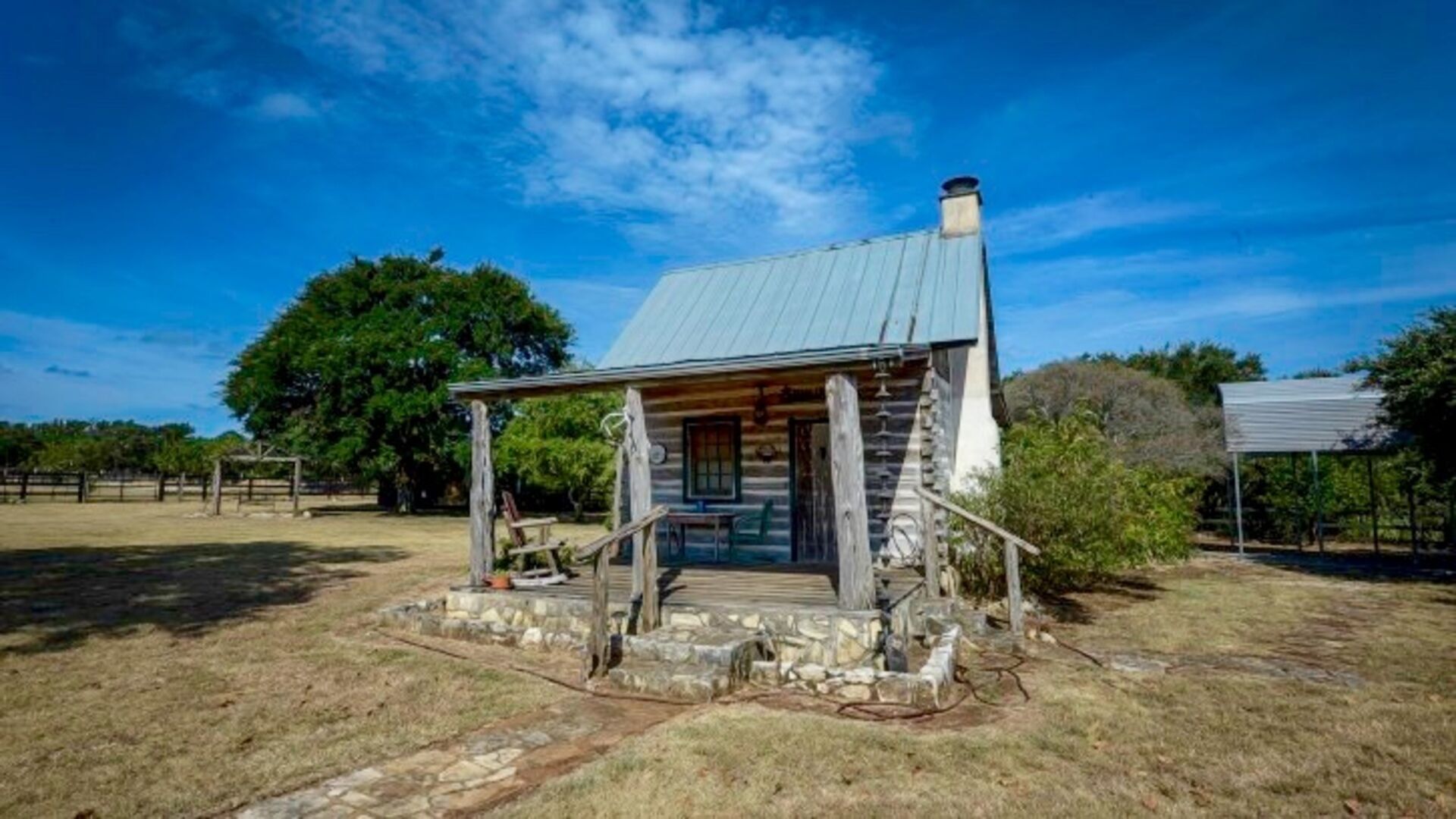 A rustic cabin with a stone foundation, wooden porch, and metal roof.