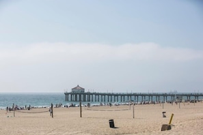 A beach with a pier extending into the water, featuring a small building at the end.