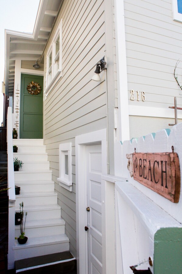 A white house with a green door, a number '216' on the wall, and a sign that says 'Beach'.