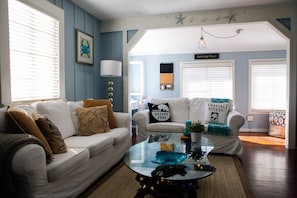 A living room with two white sofas, a glass coffee table, and a ceiling fan.