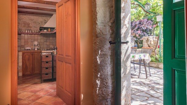 A rustic kitchen with wooden cabinets and a tiled floor, leading to an outdoor patio with a table and chairs. - Authentic Istrian House - Apartment with saltwater pool- 15 min from Kamenjak (Pula)