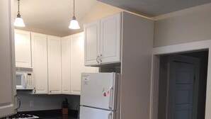 A kitchen with white cabinets, a black countertop, a refrigerator, a microwave, and a stove. - Adorable Beach Bungalow - Awesome location! Walk to beach and town! (South Haven)