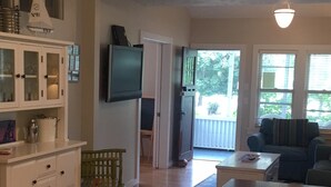 A living room with a wooden floor, a TV mounted on the wall, a dining table, and a sofa. - Adorable Beach Bungalow - Awesome location! Walk to beach and town! (South Haven)