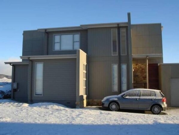 A two-story building with a garage door and a car parked in front. - Ridgefield II Luxury Home (Jindabyne)