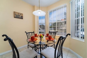 A dining area with a round glass table, black chairs, and a hanging light fixture.