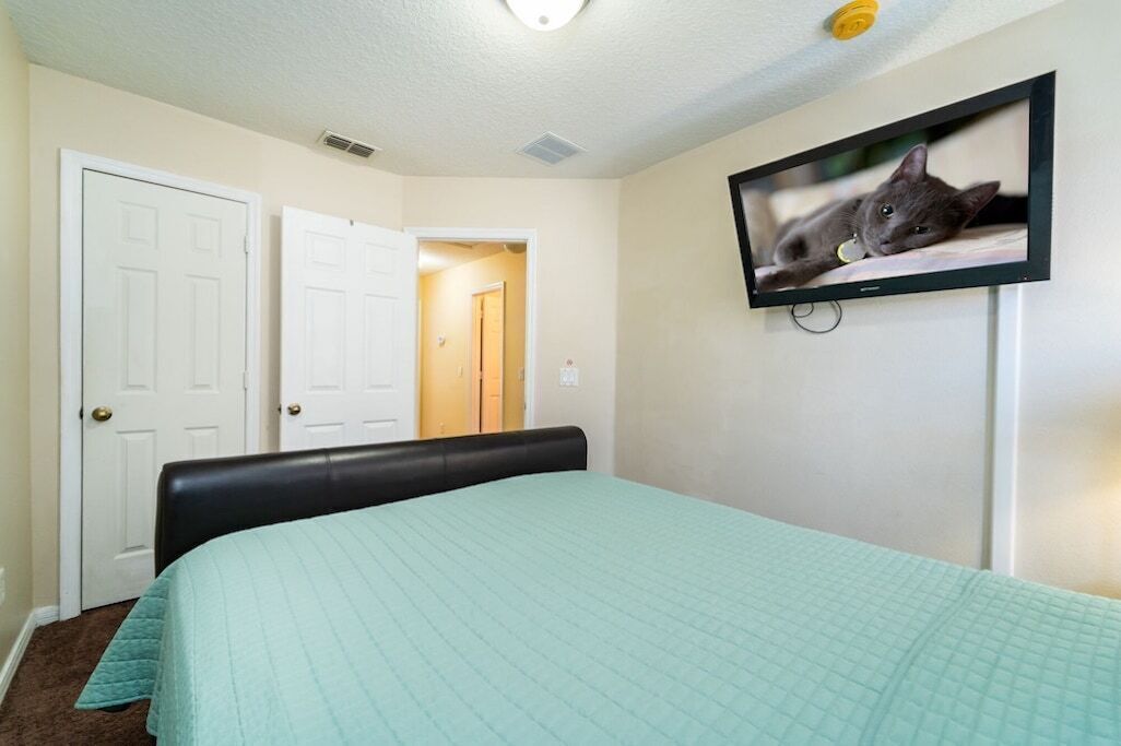 A bedroom with a bed, a television mounted on the wall, and two white doors.