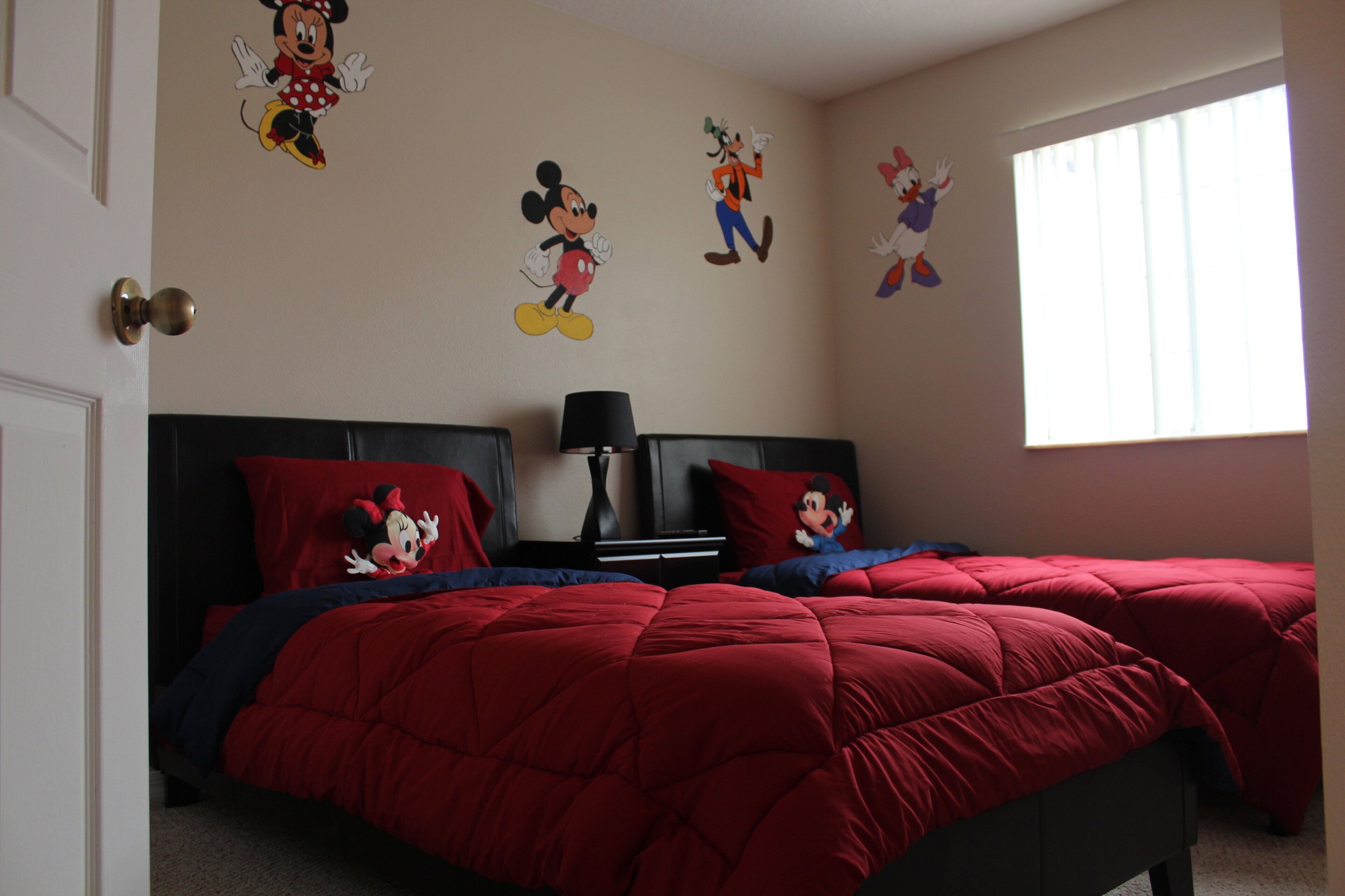 Un dormitorio con dos camas, ropa de cama roja y adhesivos de pared de Mickey Mouse.