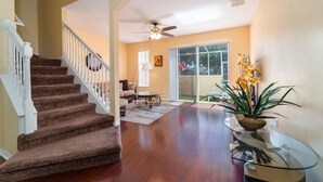 A spacious living area with a wooden staircase, a glass coffee table, and a potted plant.