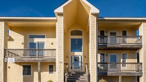 A two-story apartment building with a central entrance, a small porch, and a balcony on the ground floor. - 718 Dog-Friendly, Ocean-Side Duck w/ Private Pool (Duck)