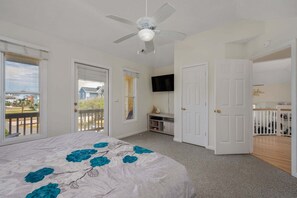 Une chambre avec un lit, un ventilateur de plafond, une télévision et un balcon.