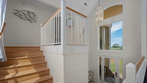 A staircase with wooden steps and white railings, a chandelier, and a view through a glass door. - 718 Dog-Friendly, Ocean-Side Duck w/ Private Pool (Duck)