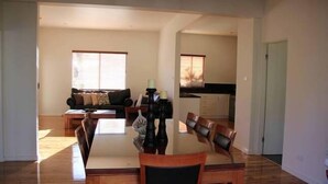 Un comedor amplio con una mesa y sillas de madera, un sofá al fondo y una cocina visible a través de un arco.