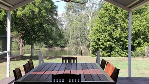 Une terrasse extérieure avec une table et des chaises, entourée d’arbres et bordée par un plan d’eau.