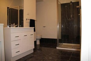 Une salle de bain avec un meuble-lavabo blanc, une cabine de douche en verre et des toilettes.