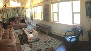 A cozy living room with a brown sofa, a wooden coffee table, and a fireplace. There is a television mounted on the wall and a window with a star decoration.